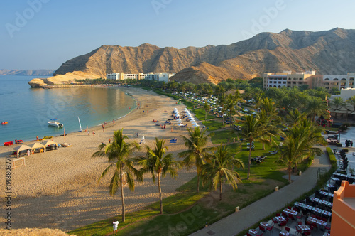 Beautiful beach surrounded by mountains and snow-white Arab buildings. Oman.