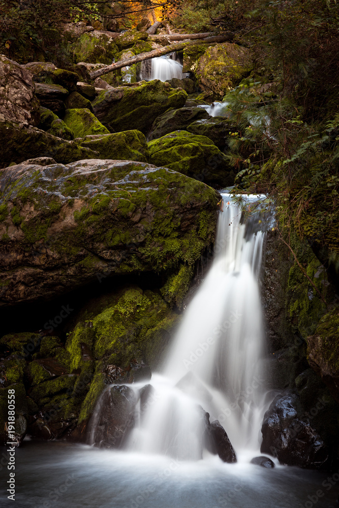Beautiful fairy mountain waterfall in a fairy forest among rocks at sunset Beautiful fairy mountain waterfall in a fairy forest among rocks at sunset