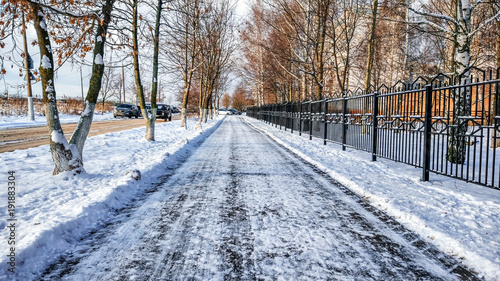 The cleared road in the park, cleaned in winter in the city, the road cleaned by a sunny day. Asphalt in the snow next to the fence. © byswat