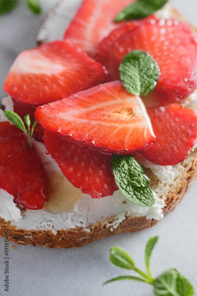 Close-up of a sweet sandwich with fresh strawberry, cream cheese, honey and mint on the white marble.