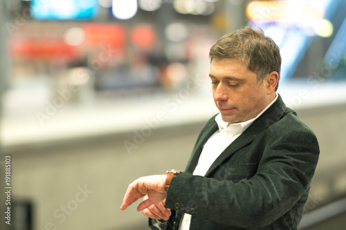 Foto Impatient traveler at station waiting for his delayed train and checking the tim