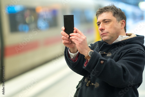 Passenger taking photos with his smartphone from railway station platform