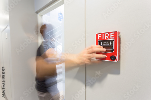 The man running and hand is pulling fire alarm on the wall next to the emergency exit door.