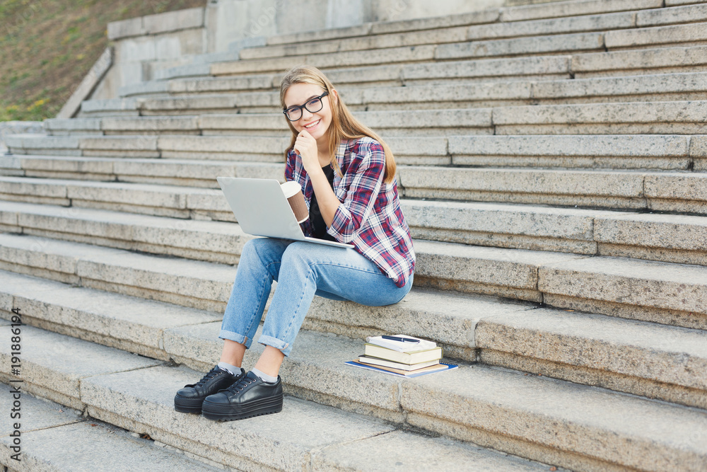 Smiling student sitting on stairs using laptop Smiling student sitting on stairs using laptop