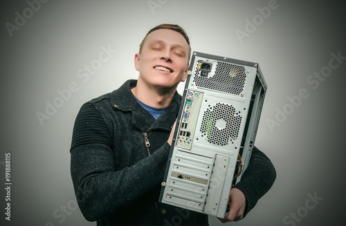 Happy computer tecnician man hugs a computer isolated on dark background. Gamer man love his computer. Computer dependent concept. photo