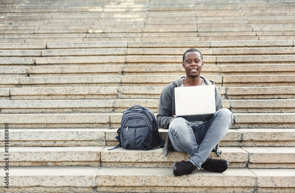 Smiling student sitting on stairs using laptop Smiling student sitting on stairs using laptop