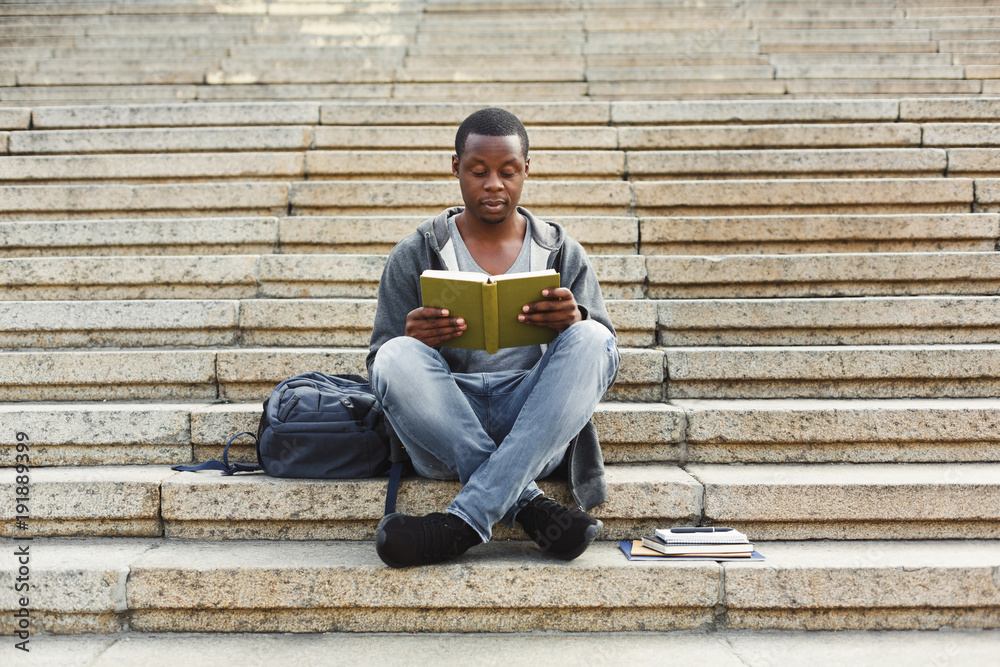 Concentrated african-american student reading book on university stairs
