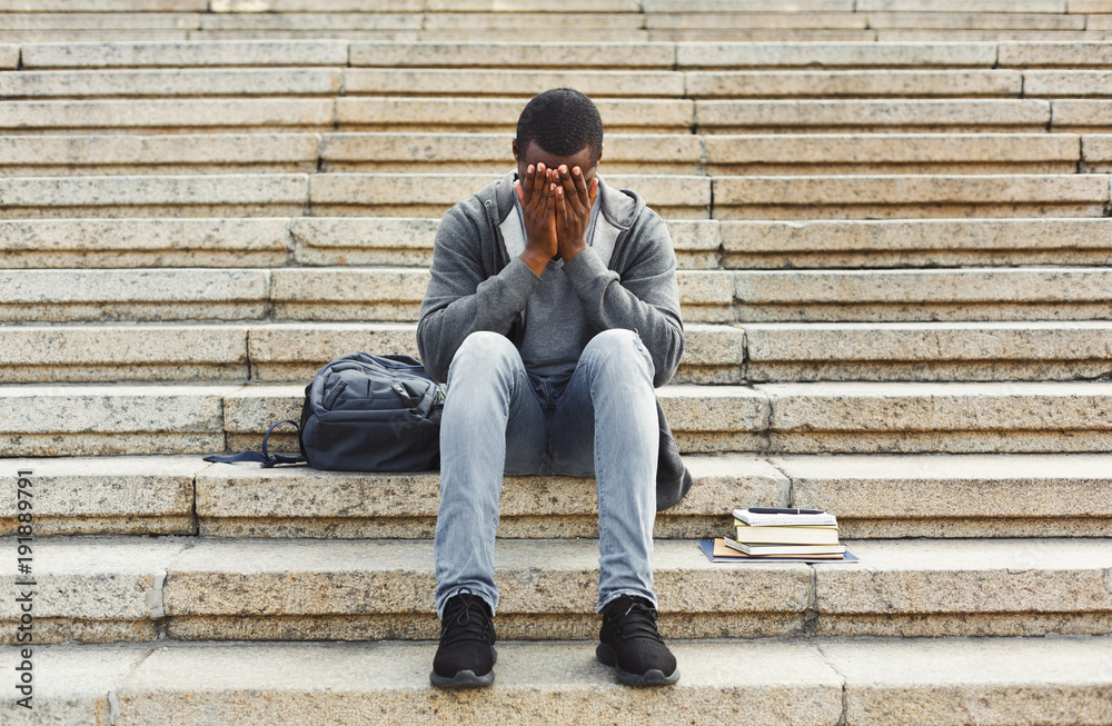 Desperate african-american student sitting on stairs outdoors Desperate african-american student sitting on stairs outdoors
