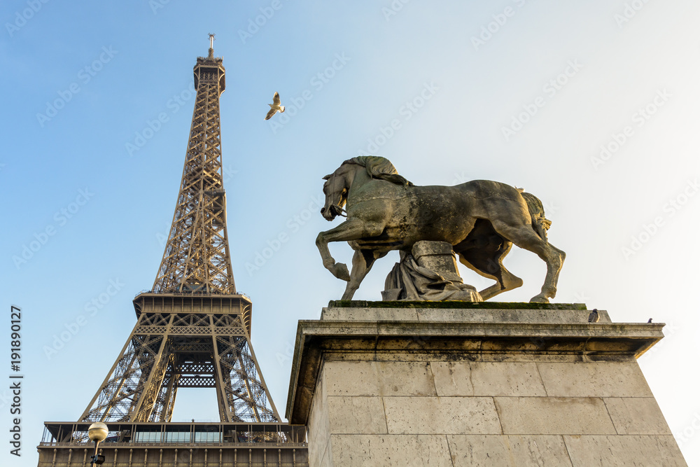 Φωτογραφία Low angle view of the Eiffel tower in Paris, seen from the Iena bridge against blue sky, with an equestrian stone statue in the foreground