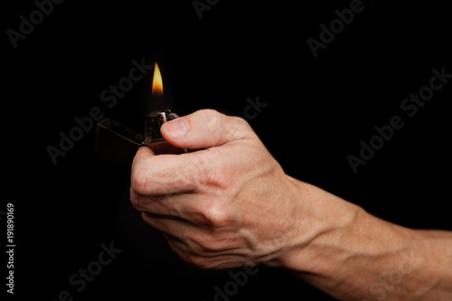 Canvastavla Closeup mans hand holding a burning metal gasoline lighter against black backgro