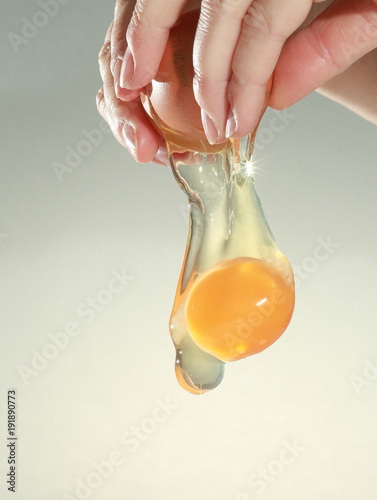 An egg is broken between fingers. the white and yolk are falling downwards