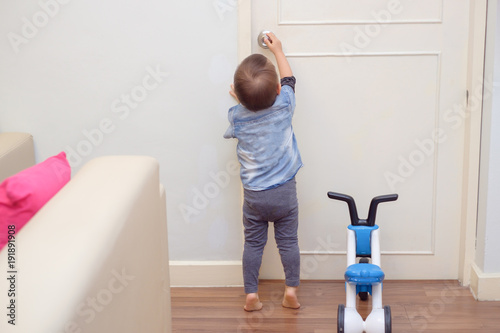Asian 18 months / 1 year old toddler baby boy standing on tiptoes at home, Kid reaching up try to open / close door knob, Child want to escape to play, explore outdoor, Security and Safety Concept