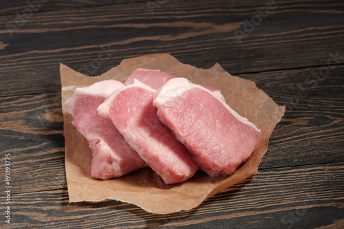 Fresh raw pork steaks on paper on a dark wooden background.