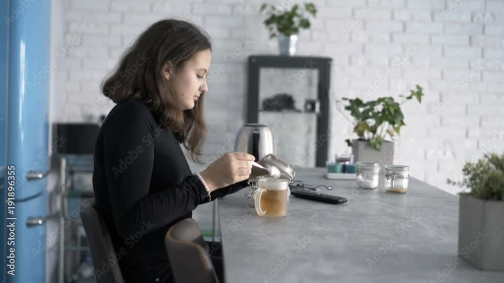 Teenage girl adding sugar into tea and mixing sitting by table at home
Teenage girl adding sugar into tea and mixing sitting by table at home