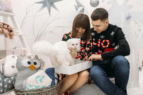 Portrait of a young couple posing with white cat in a cosy room