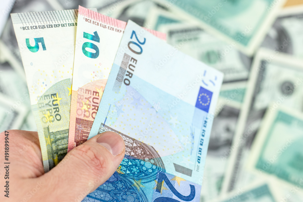 Hand holds 3 euro banknotes on dollar bills background close-up Hand holds 3 euro banknotes on dollar bills background close-up