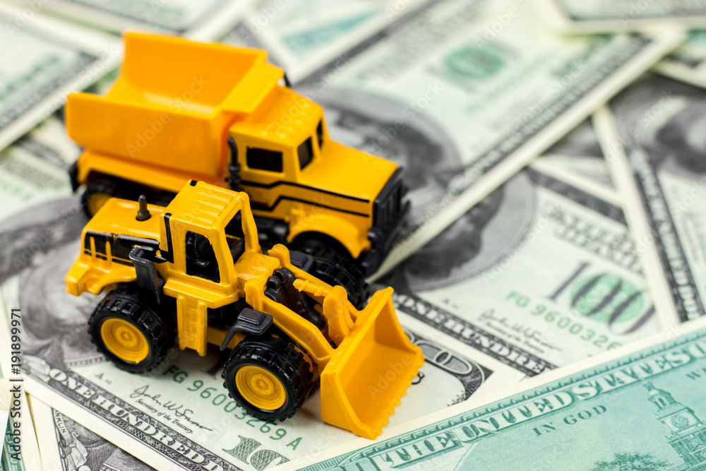 Construction vehicles for building concept. Yellow toys truck, backhoe on dollar bills background.