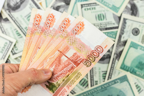 Hand holds Russian 5000 ruble banknotes on dollar bills background close-up
