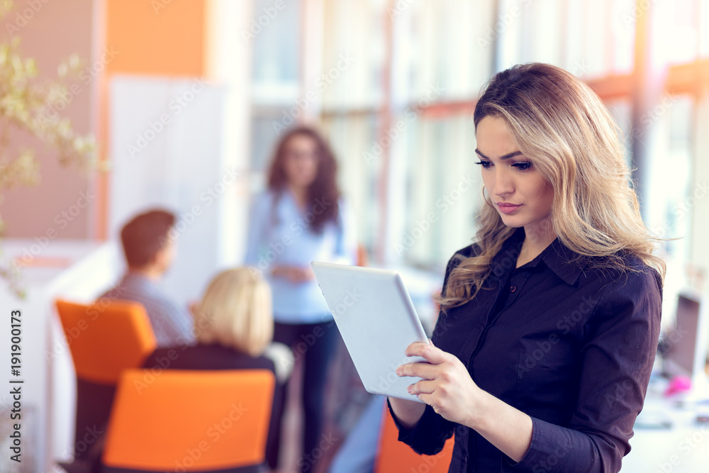 Join a digital age. Cheerful young woman holding digital tablet while his friends working on background Join a digital age. Cheerful young woman holding digital tablet while his friends working on background