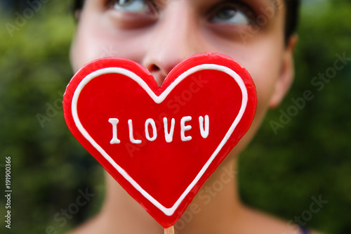 Elegant young woman holding heart shaped lollipop. Beautiful happy woman holds big red heart . Valentine day concept. Sweet food. Portrait of cheerful young girl eating a lollipop. photo