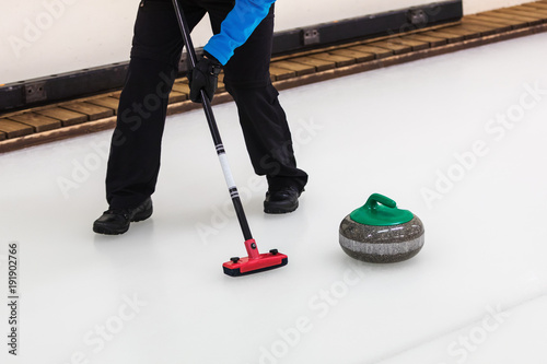 curling sport - player with broom sweeping the ice before stone