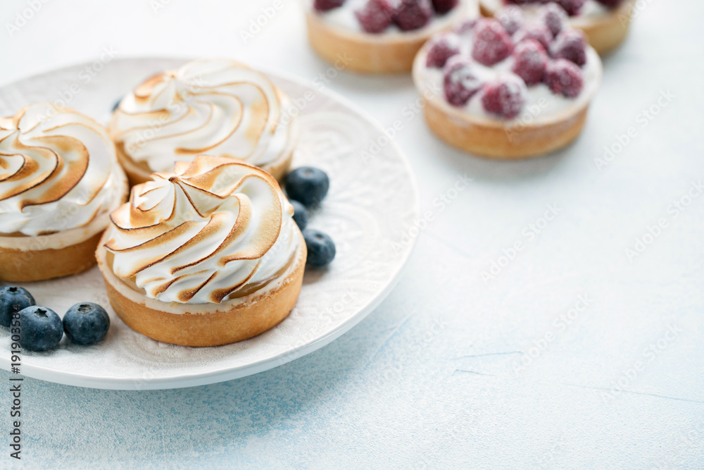 Delicious lemon and raspberry tartlets with meringue on a white vintage plate. Sweet treat on a light blue background