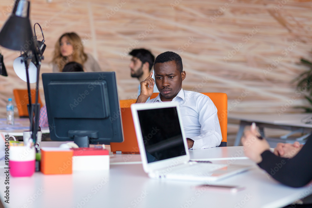 Frustrated young african entrepreneur with sad grimace in front of his laptop in office Frustrated young african entrepreneur with sad grimace in front of his laptop in office