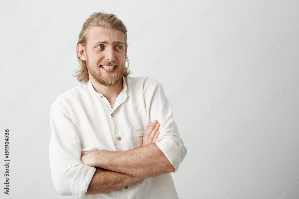 Charming blond male with stylish haircut standing with crossed hands, bending backwards, expressing disgust and dislike, frowning over gray background. Friend pokes jellyfish right in face Charming blond male with stylish haircut standing with crossed hands, bending backwards, expressing disgust and dislike, frowning over gray background. Friend pokes jellyfish right in face