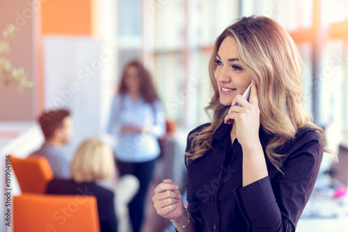 Young attractive businesswoman talking on mobile phone in office, her colleagues on the background photo