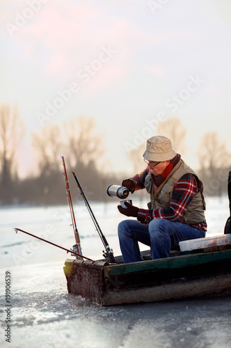 Ice fishing. elderly man sitting on frozen lake and drink tea