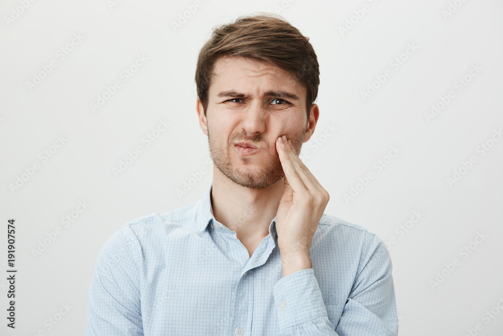 Portrait of handsome young man holding hands over chin, expressing fright and being terrified by something he sees, standing against gray background. Guy can not calm down after witnessing crime scene Portrait of handsome young man holding hands over chin, expressing fright and being terrified by something he sees, standing against gray background. Guy can not calm down after witnessing crime scene