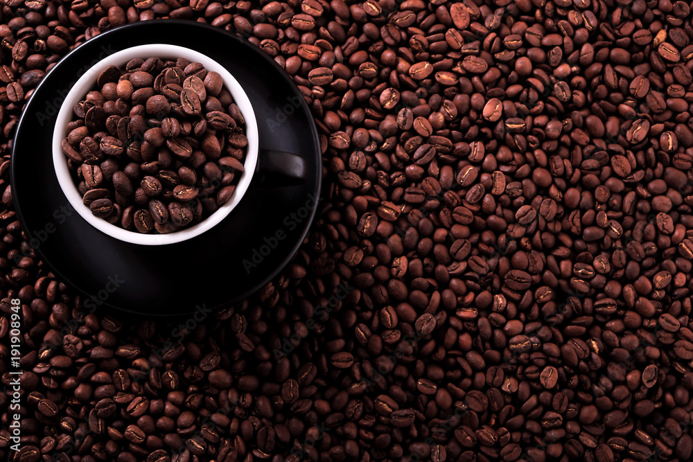 Fototapeta premium Black coffee cup and saucer one single for espresso or capuccino filled full of coffee beans on a background of scattered dark coffee beans photo
