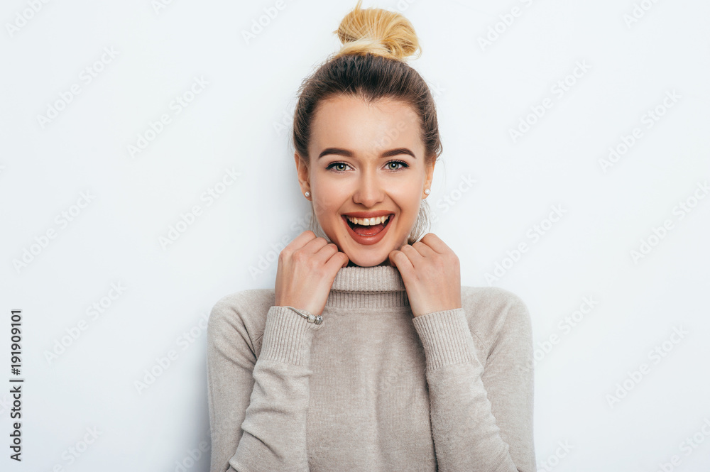 Smiling positive female with attractive look and lips wearing in sweater posing against white wall. Happy woman with hair bun showing positive emotions. People Lifestyle Beauty Fashion concepts Smiling positive female with attractive look and lips wearing in sweater posing against white wall. Happy woman with hair bun showing positive emotions. People Lifestyle Beauty Fashion concepts