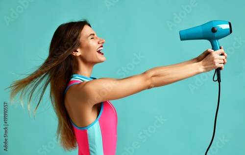 Happy young brunette woman with hair dryer on blue mint background