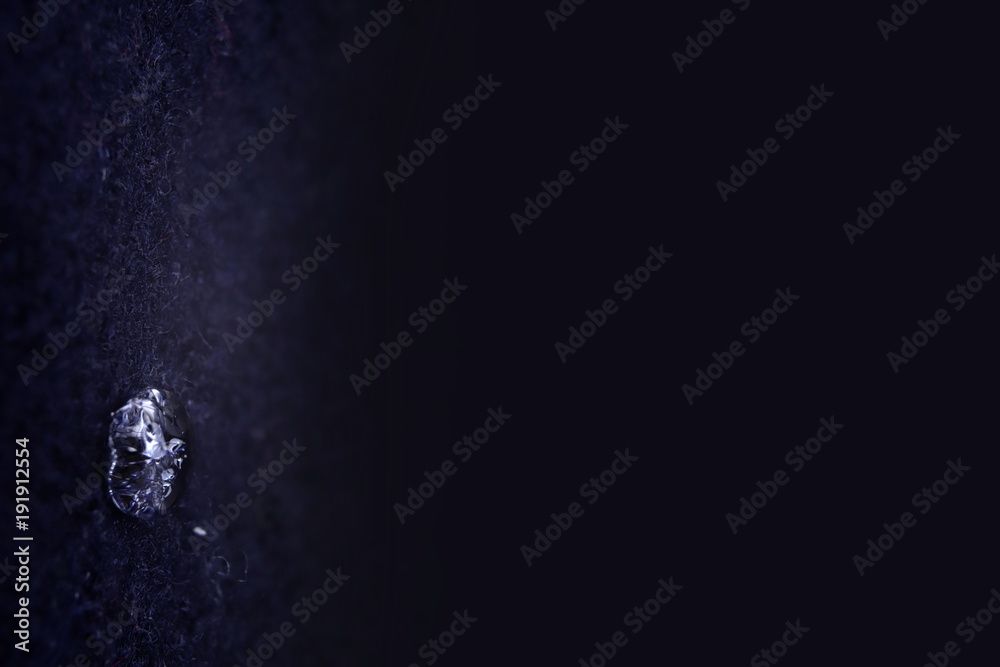 Φωτογραφία close-up of sparkling drop of water on dark blue boild wool faded to dark blue f