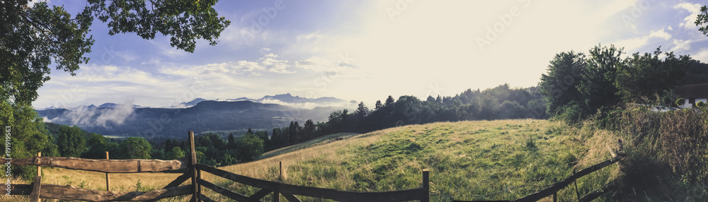 Panorama von Wiesen und Bergen mit einem Holzzaun im Vordergrund