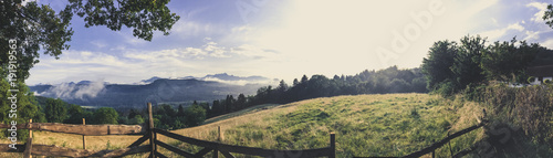 Panorama von Wiesen und Bergen mit einem Holzzaun im Vordergrund © Creativens