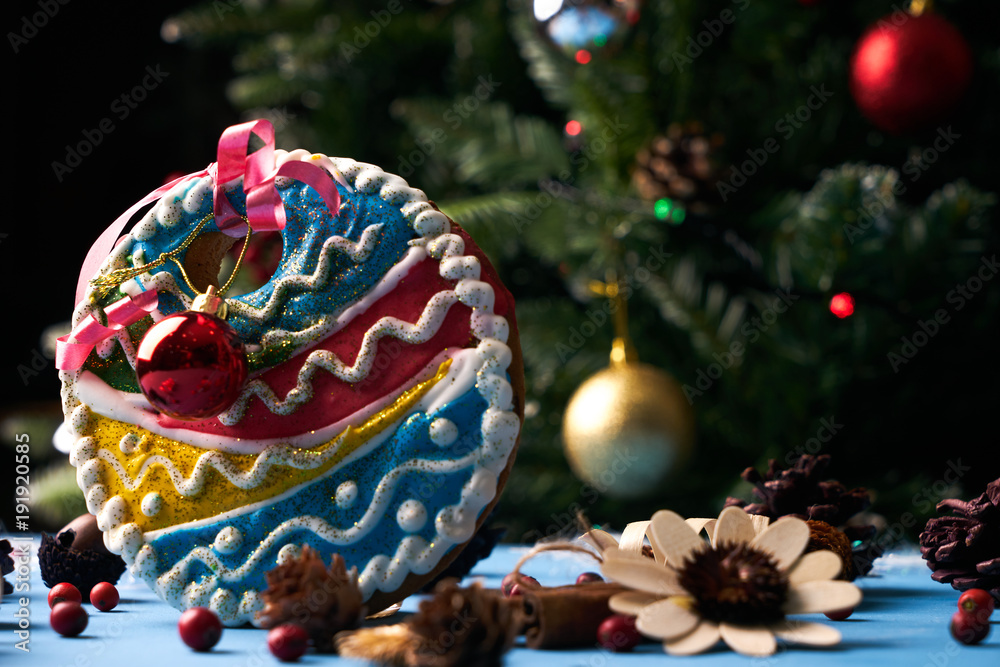 Homemade gingerbread ball cookie with festive decoration under the Christmas fir tree with garlands and colorful christmas tree bauble on background