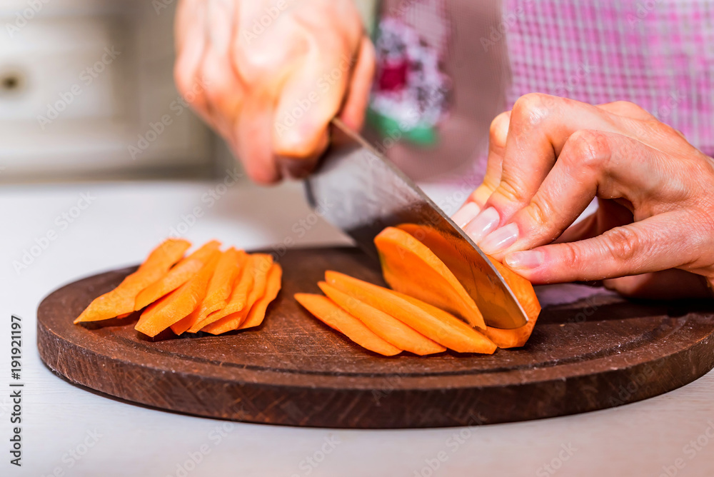 Woman's hands slice carrot on wooden board