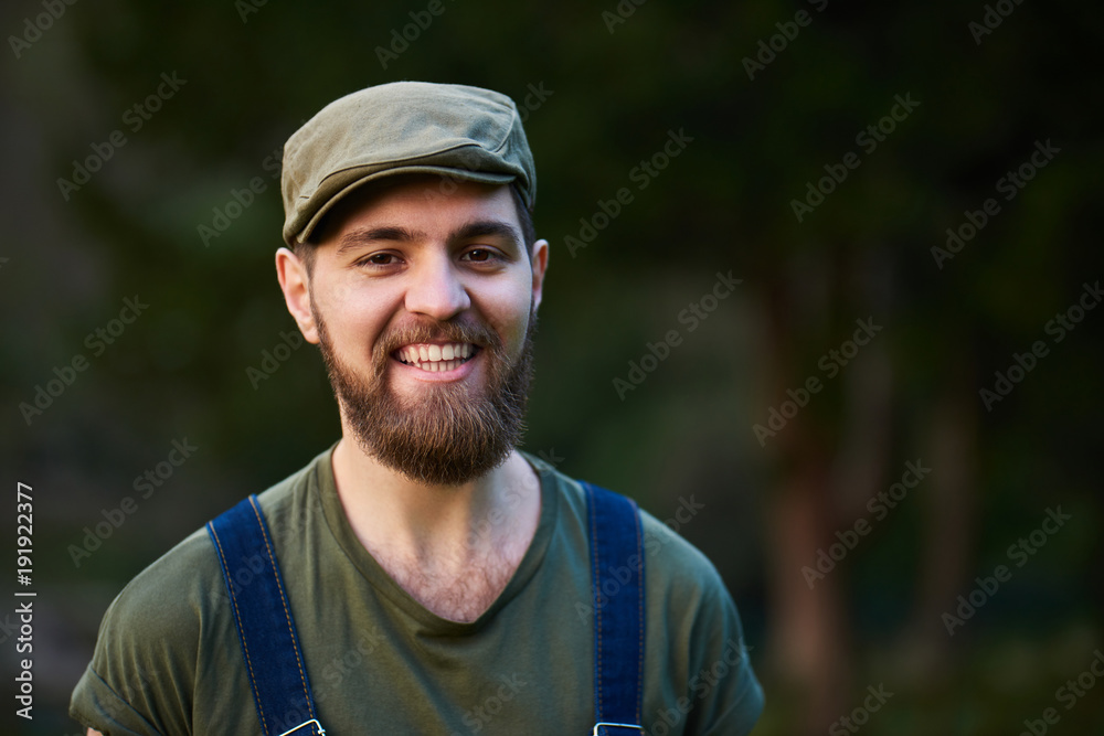 Handsome smiling bearded man in green hat in garden