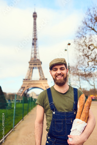 Handsome smiling bearded man holding baguette in hands over Eiffel Tower background. Paris, France