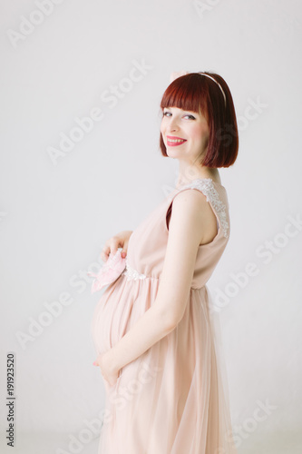 Pregnant girl is standing with pink shoes of baby