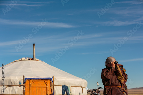 A Mongolian nomad scans the distant horizon with a monocular, looking for members of her family returning to the camp.