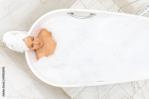 красивая молодая женщина с полотенцем на голове принимает ванну с пеной