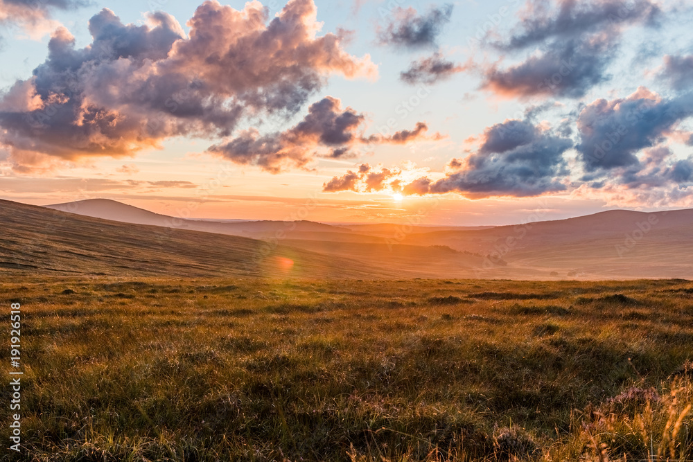 Beautiful sunset with cloudy sky and lens flare on a grass covered Hill in Glendalough, Wicklow Mountains, Ireland, slight rain, hdr Beautiful sunset with cloudy sky and lens flare on a grass covered Hill in Glendalough, Wicklow Mountains, Ireland, slight rain, hdr