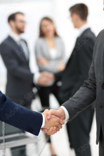 Fototapeta Naklejka Na Ścianę i Meble -  Two businessmen shaking hands with colleagues  on background.