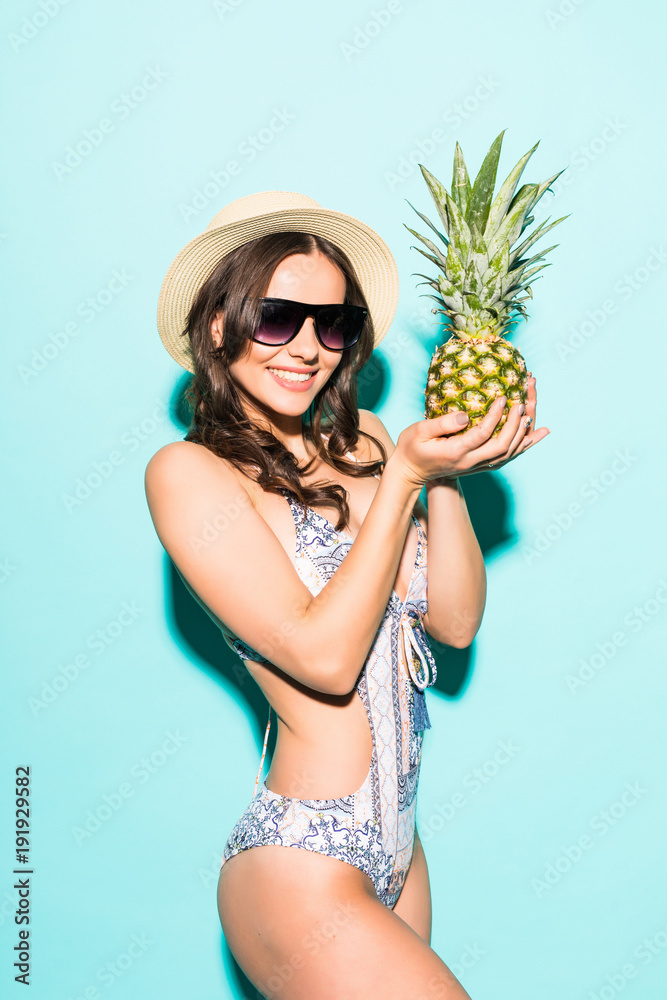 Summer girl. young woman in bikini in sunglasses and hat in yellow background holding pineapple on green background Summer girl. young woman in bikini in sunglasses and hat in yellow background holding pineapple on green background
