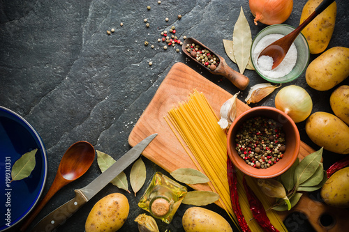 Ingredients for cooking: potatoes, salt, pepper, onion, garlic on a dark stone table. photo