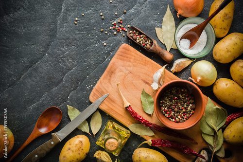 Ingredients for cooking: potatoes, salt, pepper, onion, garlic on a dark stone table. photo