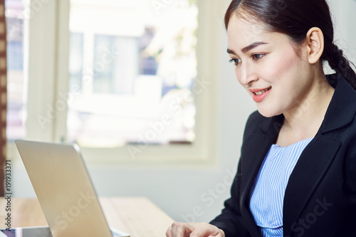 Smiling business woman in black suit is sitting working on laptop in office. Happy work concept.